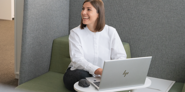 Projektleiterin Patricia aus dem Immobilienbereich sitzt in einer Sitzecke im Büro am Laptop und lacht zur Seite.