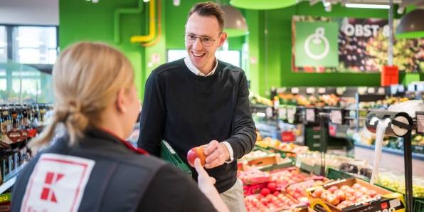 Hausleiter einer Kaufland-Filiale reicht einer Mitarbeiterin einen Apfel.