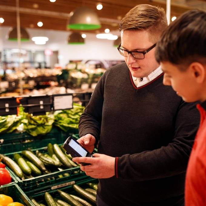 Vor dem Gemüsestand: Kaufland-Filialleiter, der ein Scan-Gerät in den Händen hält, im Gespräch mit einem Mitarbeiter.