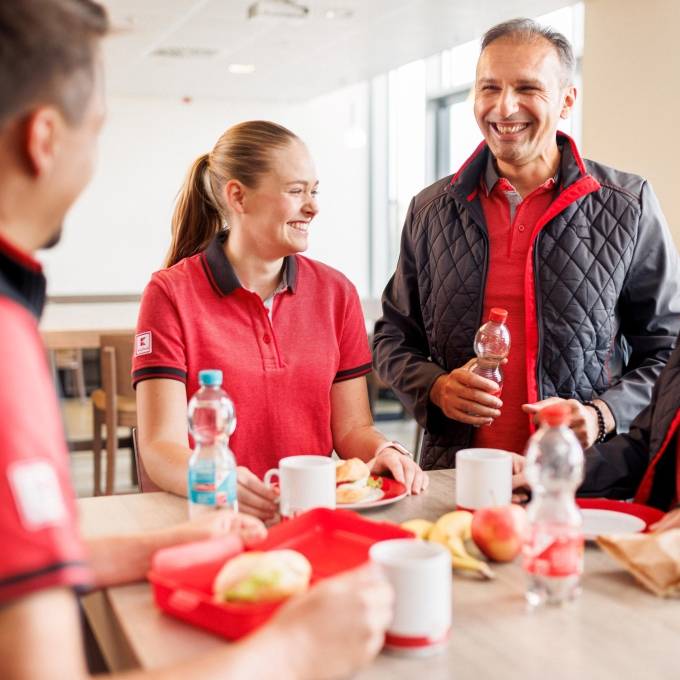 Vier Logistikmitarbeiter von Kaufland gut gelaunt bei der Mittagspause im Pausenraum eines Logistikzentrums.