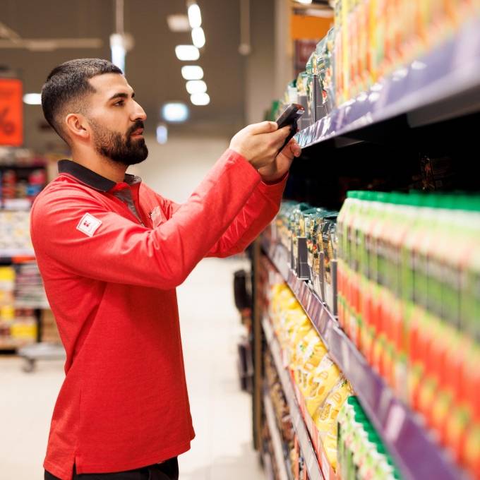 Ein Mitarbeiter in roter Kaufland-Kleidung steht in einem Gang und scannt Ware.