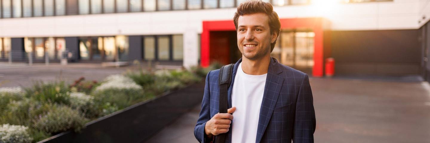 Feierabendstimmung: Ein Mitarbeiter auf dem Heimweg. Die Abendsonne spiegelt sich im Hintergrund auf der Fassade eines Kaufland-Bürogebäudes.