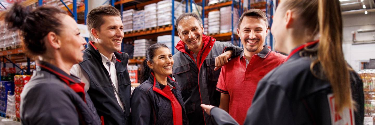 Sechs Logistikmitarbeiter von Kaufland im Gespräch. Im Hintergrund volle Lagerregale.