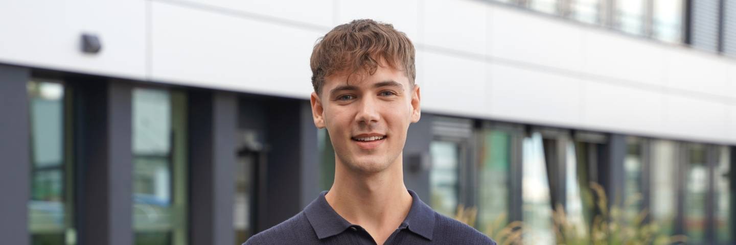 Dualer Student steht vor einem Bürogebäude von Kaufland und lächelt freundlich in die Kamera