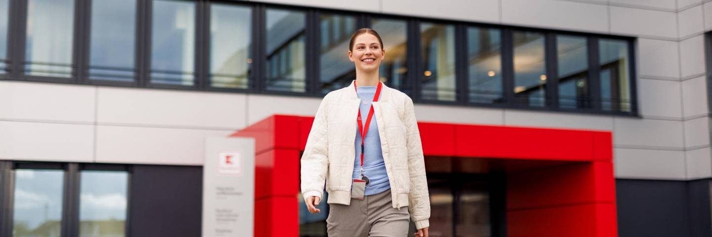 Ein Azubi, eine junge Frau in heller Jacke, entfernt sich vom Haupteingang der Kaufland-Zentrale.