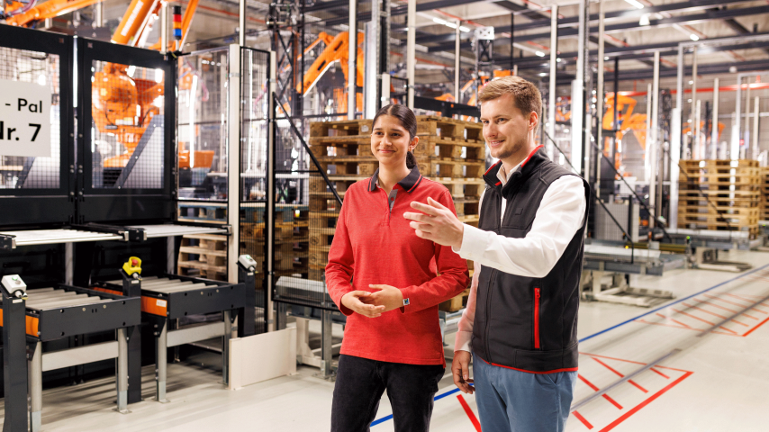 Eine junge Mitarbeiterin und ein Ausbilder arbeiten in der Logistik. Der Ausbilder erklärt etwas.