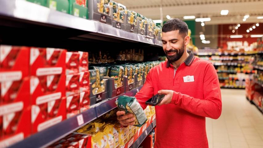 Ein Mitarbeiter in roter Kaufland-Kleidung steht in einem Gang und scannt eine Packung Nudeln.