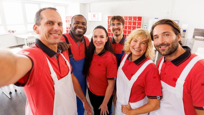 Ein Kaufland-Fleischwerk-Mitarbeiter macht mit seinen Kollegen ein Gruppenselfie im Pausenraum eines Kaufland-Fleischwerks.