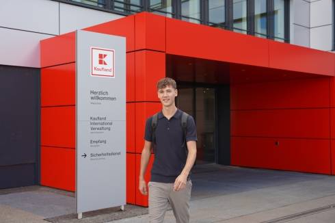 Dualer Student läuft aus dem Bürogebäude von Kaufland International und lächelt freundlich.