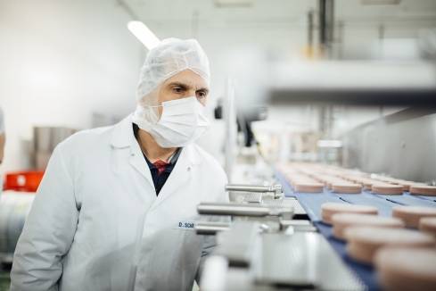 Mit Mundschutz und in Arbeitskleidung: Der Teamleiter im Kaufland-Fleischwerk wirft am Band einen prüfendem Blick auf die Ware.