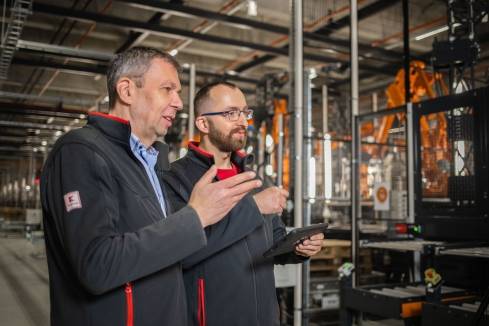 Teamleiter für Automatisierungstechnik erklärt einem Mitarbeiter etwas und zeigt mit der Hand auf eine Anlage.