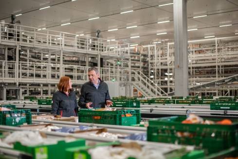 Teamleiter in der Logistik läuft durch den Frische-Bereich eines halbautomatisierten Logistikzentrums und erklärt der Nachwuchskraft etwas.