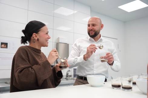 Zwei Mitarbeiter bei Kaufland International verkosten gemeinsam Kaffee und lächeln sich an.