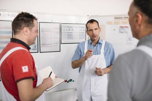3 Kaufland-Fleischwerk-Mitarbeiter in der Besprechung. Ein Mitarbeiter macht sich Notizen.