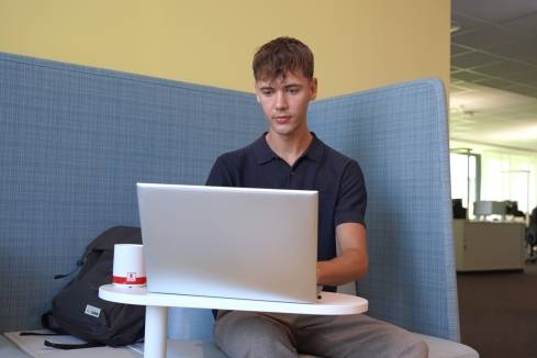 Dualer Student sitzt auf einem blauem Sofa und arbeitet konzentriert an einem Laptop.