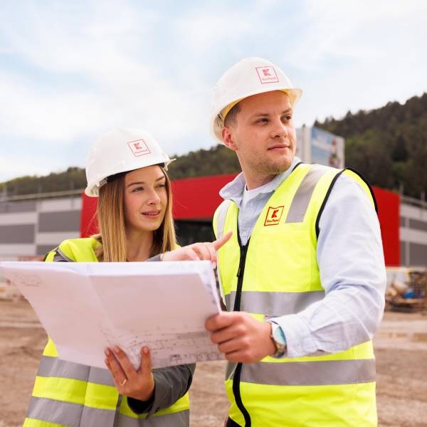 Zwei Mitarbeiter stehen vor dem Bau eines Kaufland-Marktes und schauen einen Bauplan an.