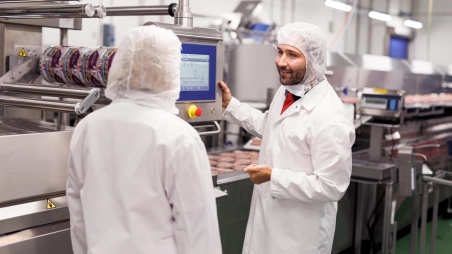 Fertigungsanlage in einem Kaufland-Fleischwerk. Zwei Kaufland-Mitarbeiter bedienen eine Produktionsanlage und unterhalten sich.