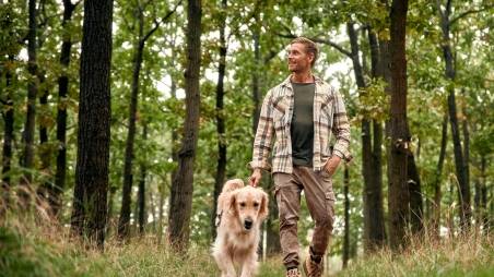 Mann geht mit Hund im Wald spazieren.