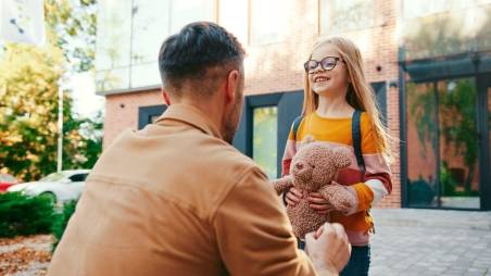 Vater steht mit Tochter draußen vor einem Gebäude.