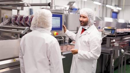 Fertigungsanlage in einem Kaufland-Fleischwerk. Zwei Kaufland-Mitarbeiter bedienen eine Produktionsanlage und unterhalten sich.