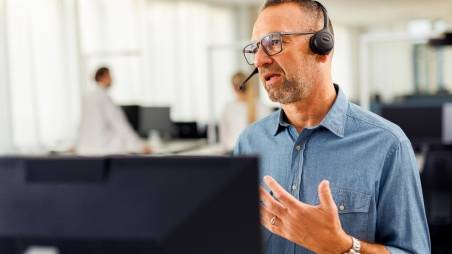 Kaufland-Mitarbeiter mit Headset vor einem Bildschirm in angeregtem Gespräch bei einer Telko.