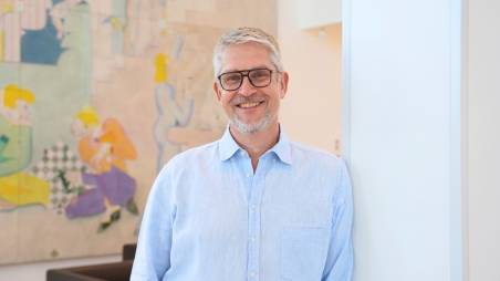 Porträt des lächelnden Managers Knut Harenkamp mit Brille und hellem Hemd, stehend vor einem modernen, farbigen Kunstwerk (Kaufland Karriere).