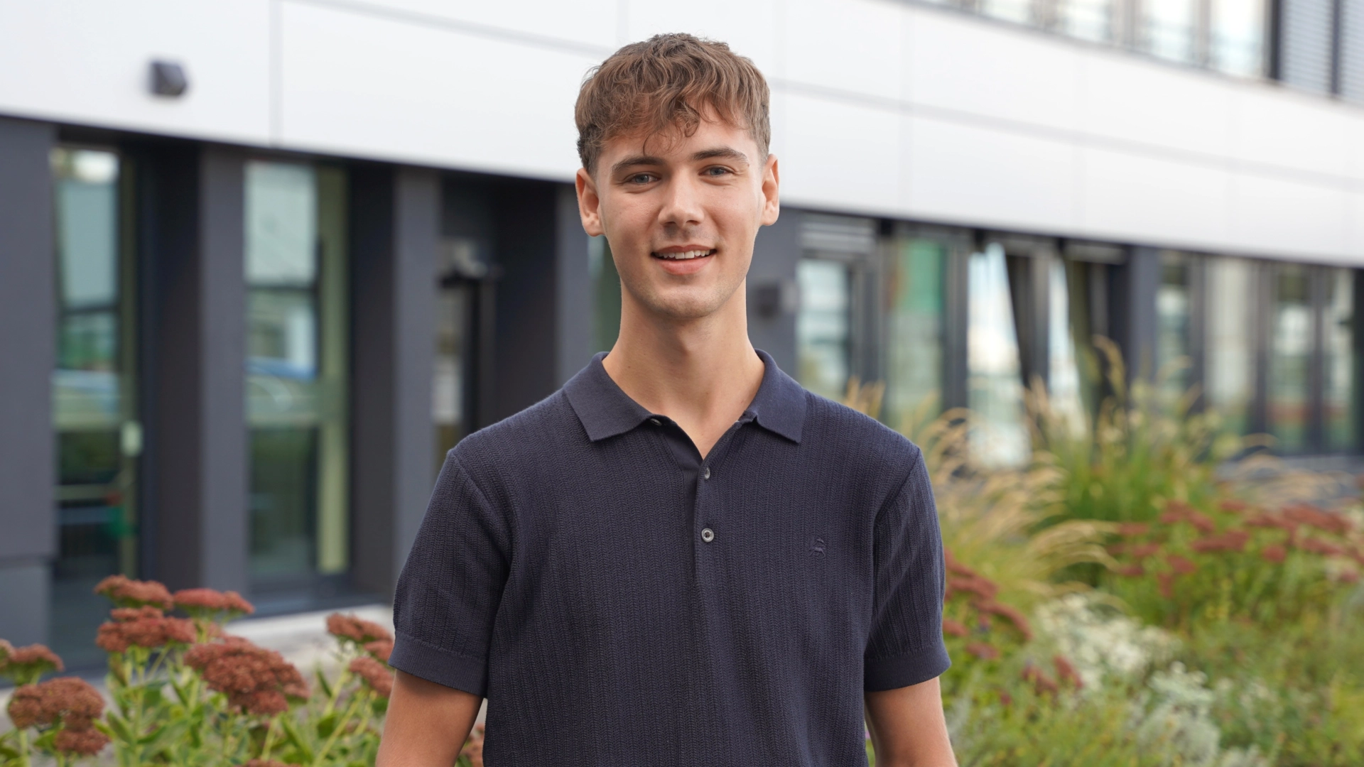 Dualer Student steht vor einem Bürogebäude von Kaufland und lächelt freundlich in die Kamera