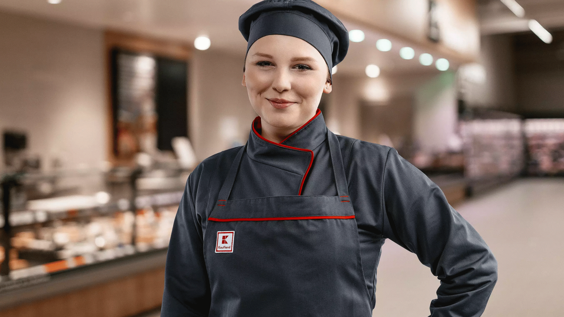 Auszubildende bei Kaufland steht vor einer Bedientheke und lächelt in die Kamera.