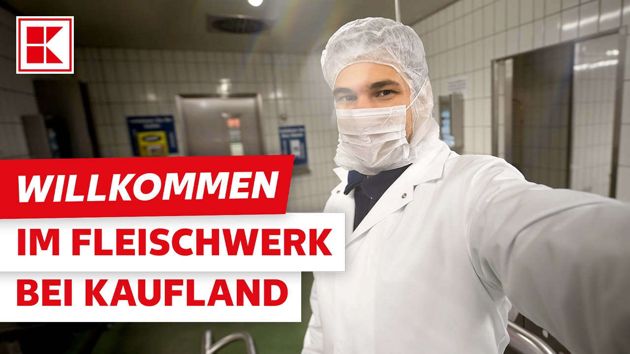 Ein lächelnder Mitarbeiter von Kaufland in hygienischer Schutzkleidung (Haube, Mundschutz, weißer Kittel) macht ein Selfie in einem sterilen Fleischwerk. Das Video heißt "WILLKOMMEN IM FLEISCHWERK BEI KAUFLAND".