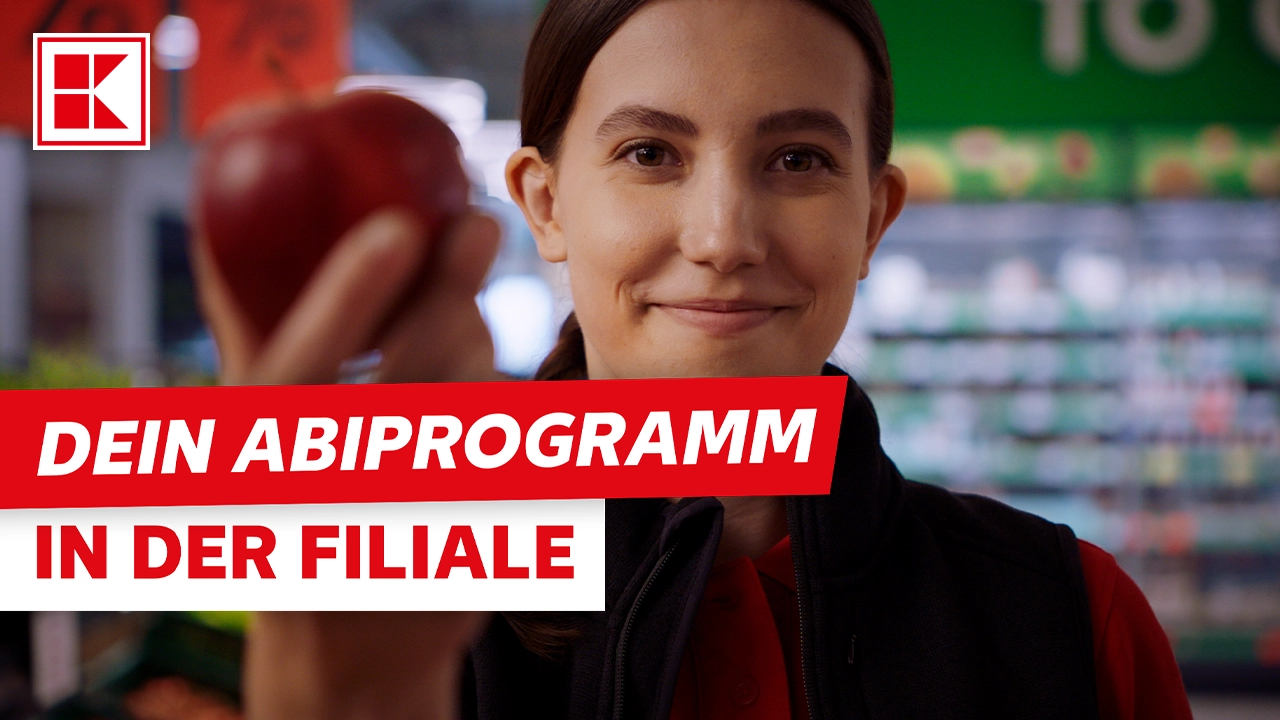 Eine lächelnde Mitarbeiterin hält in der Filiale einen Apfel. Der Text "DEIN ABIPROGRAMM IN DER FILIALE" ist eingeblendet.